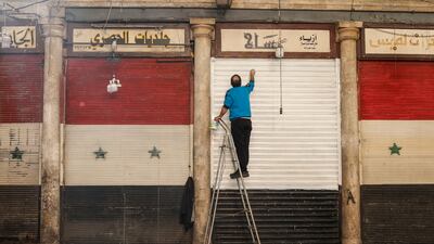A man repaints his storefront in Damascus, daubing over the flag of the former Syrian government. EPA