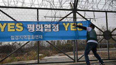 A pro-unification activist puts up a banner reading 'Yes end-of-war declaration, Yes peace treaty' on a fence near the Demilitarised Zone dividing the two Koreas. AFP