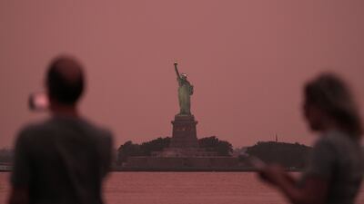 People take photographs of the Statue of Liberty at sunset through haze caused by smoke from Canadian wildfires, in New York City, US. Reuters