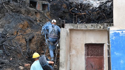 Work is being carried out to restore essential services as men walk with electric cables through the charred remains of trees after a forest fire near the town of Melloula. AFP