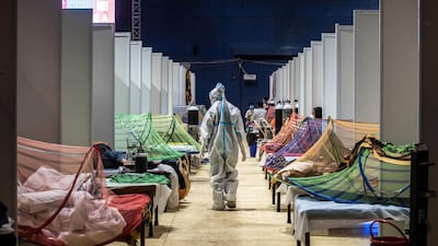 A medical worker in PPE observes patients who have been infected by Covid-19 inside a makeshift covid care facility in a sports stadium at the Commonwealth Games Village in New Delhi. Getty Images